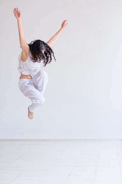 Mujer joven realizando danza contemporánea en un estudio blanco