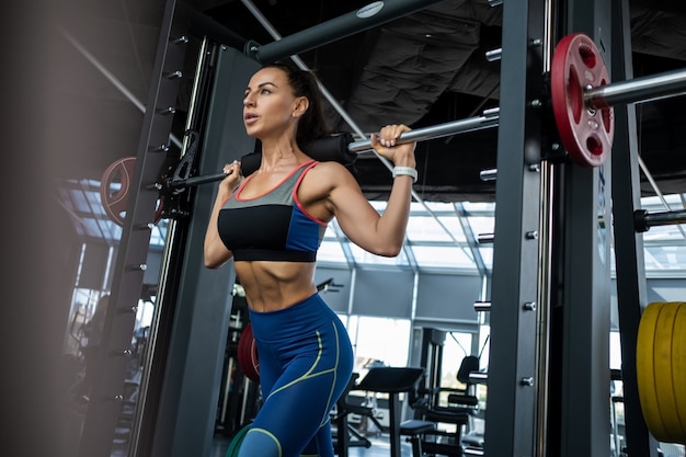 Mujer joven realizando estocadas en la máquina Smith en el gimnasio