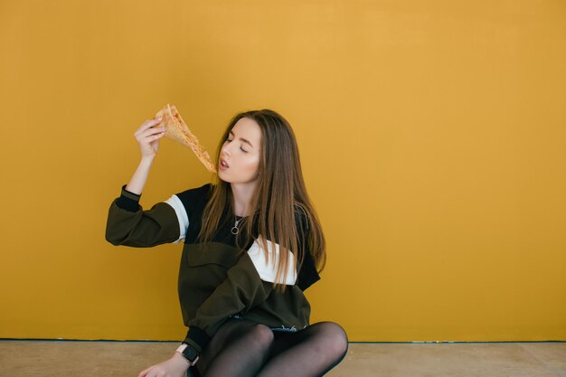 Mujer joven con rebanada de deliciosa pizza sobre fondo de color