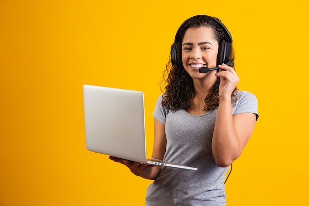 Mujer joven recepcionista que trabaja con portátil y auriculares.