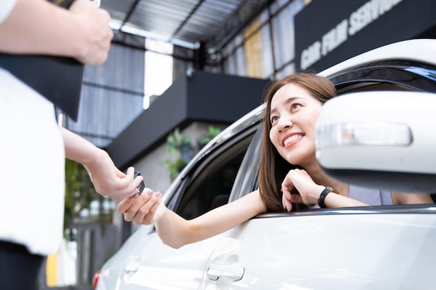 Mujer joven recibe una llave de la sala de exposición de automóviles después de realizar el contrato de compra de un automóvil.