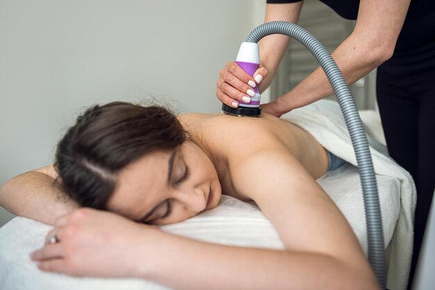 Mujer joven recibe masaje anticelulítico en la espalda con un dispositivo de vacío de hardware en el spa