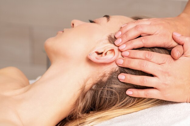 Foto mujer joven recibiendo masaje de cabeza por manos de esteticista en salón de belleza spa