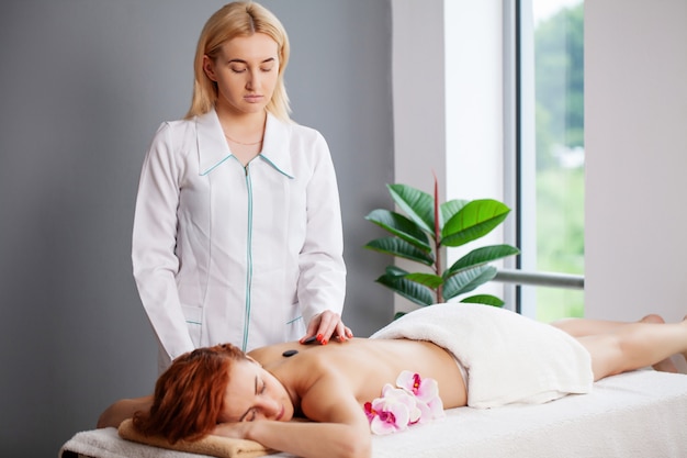 Mujer joven recibiendo masaje con piedras calientes en el salón de spa.