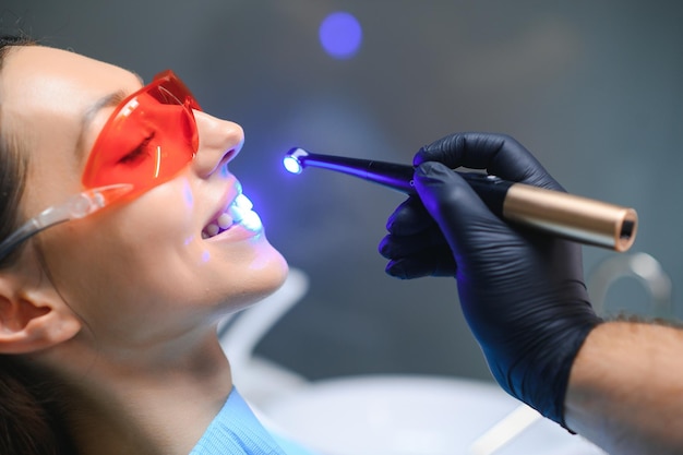 Mujer joven recibiendo un procedimiento de secado de rellenos dentales con luz UV curativa en una clínica dental