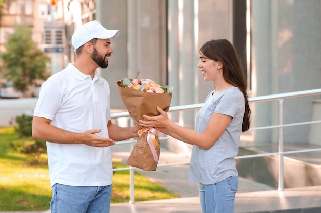 Mujer joven recibiendo ramo de flores de mensajería al aire libre