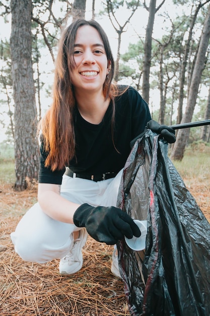Una mujer joven recoge basura abandonada en una bolsa negra en el bosque Contaminación plástica y protección ambiental Problema de la ecología de la cama y la contaminación ambiental con desechos en descomposición prolongada