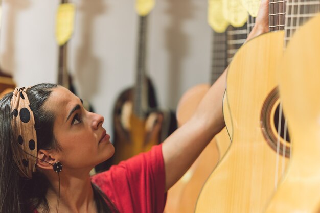 Mujer joven recogiendo una guitarra colgada en una tienda con otras guitarras.