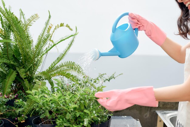 Mujer joven regando plantas en el jardín de su balcón de la ciudad