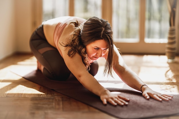 Mujer joven relajada haciendo ejercicio de estiramiento mientras practica yoga en casa.