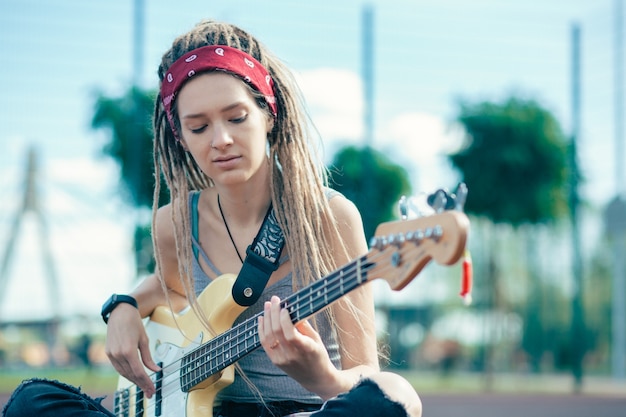 Mujer joven relajada tranquila con rastas tocando la guitarra pensativamente mientras está sentado en el suelo