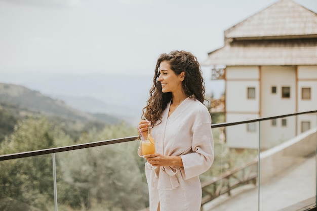 Mujer joven relajándose y bebiendo jugo de naranja fresco en la terraza al aire libre