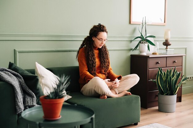 Mujer joven relajándose y comprando en línea con un teléfono inteligente en casa Mujer feliz disfrutando de las redes sociales en el teléfono móvil en casa Mujer atractiva usando un teléfono inteligente para entretenimiento y comunicación