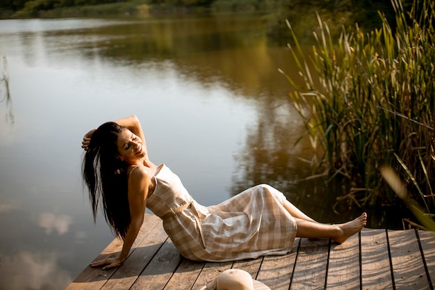 Mujer joven relajándose en el muelle de madera en el lago tranquilo en un caluroso día de verano