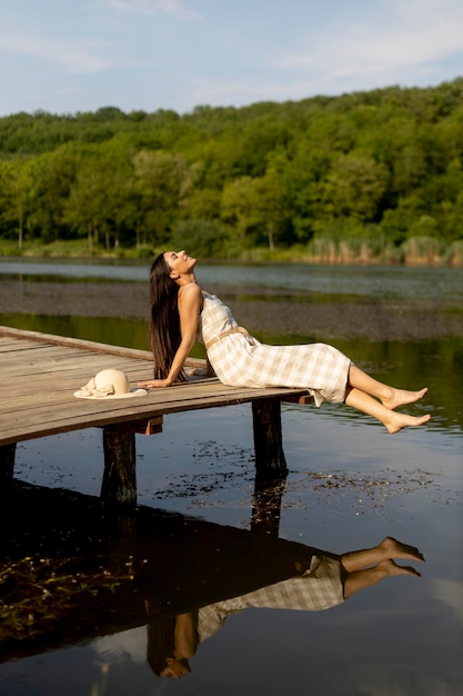 Foto mujer joven relajándose en el muelle de madera en el lago tranquilo