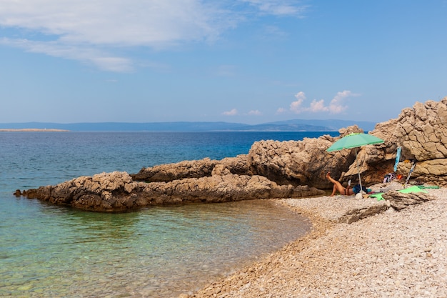 Mujer joven relajándose bajo la sombrilla en la playa de Stara Baska