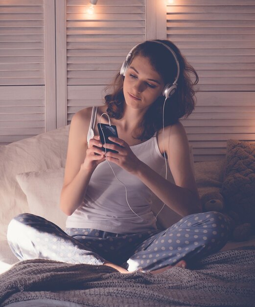 Mujer joven relajándose en su cama está escuchando música