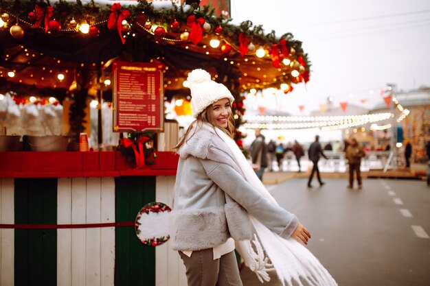 Mujer joven relajante bebiendo café en la feria festiva de Navidad Vacaciones de invierno Luces alrededor