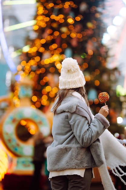 Mujer joven relajante bebiendo café en la feria festiva de Navidad Vacaciones de invierno Luces alrededor