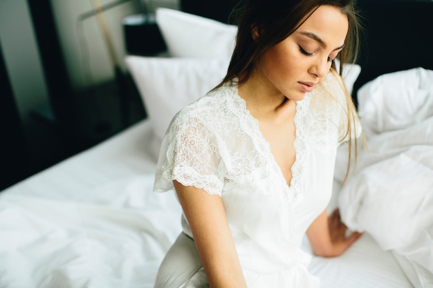 Mujer joven relajante en cama blanca después de despertarse