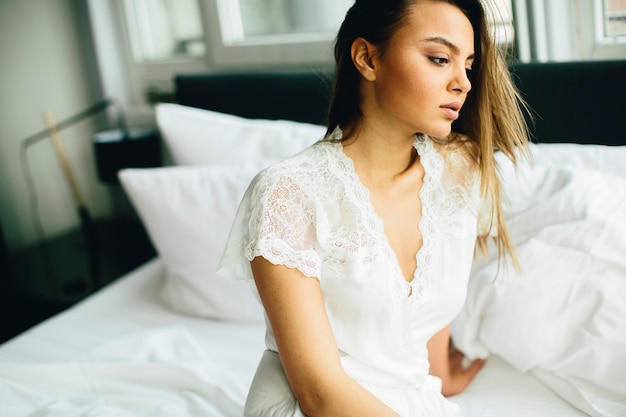 Mujer joven relajante en una cama blanca en la mañana