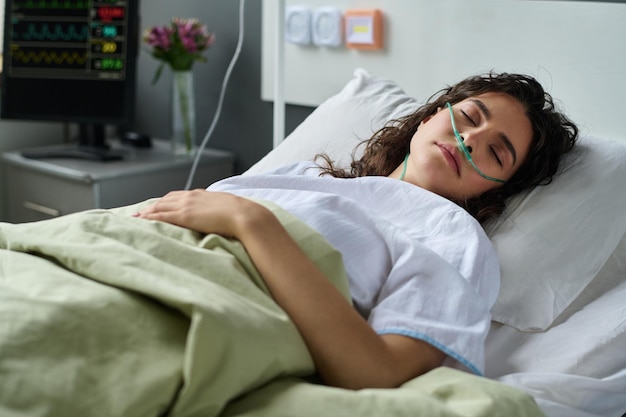 Mujer joven respirando con un tubo de oxígeno especial acostado en la cama en la sala del hospital