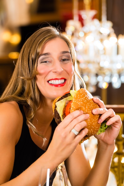 Foto mujer joven: un restaurante de alta cocina come una hamburguesa, se comporta incorrectamente