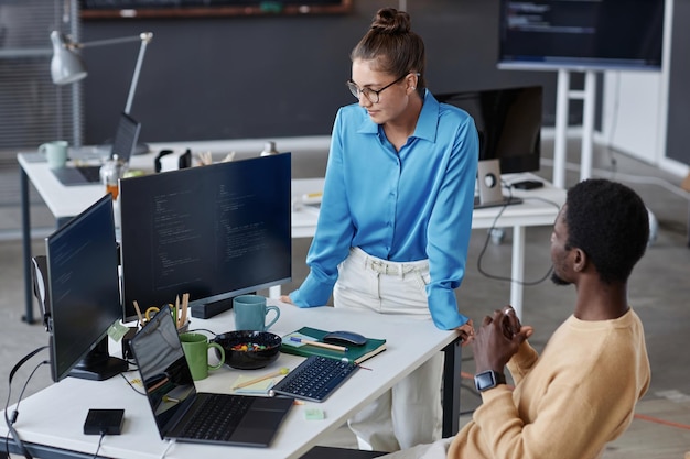 Mujer joven revisando los códigos informáticos de su colega mientras desarrolla nuevo software en la oficina