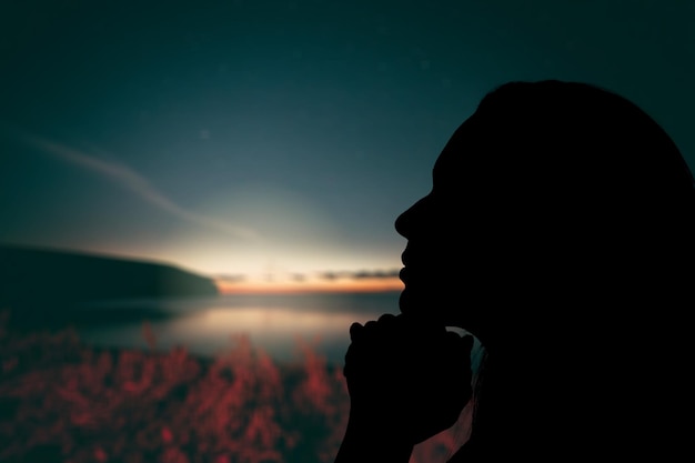 Mujer joven rezando sobre fondo puesta de sol