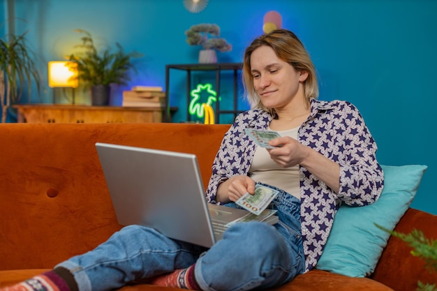 Mujer joven rica feliz independiente contando dinero en efectivo uso de computadora portátil planificación del presupuesto del hogar