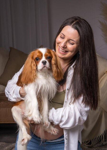 Una mujer joven se ríe alegremente y juega con su perro Cavalier King Charles Cocker Spaniel