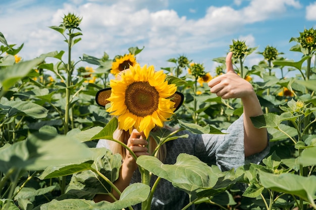 Mujer joven se ríe con girasol en su rostro retrato sin rostro de mujer joven en sombrero de paja con