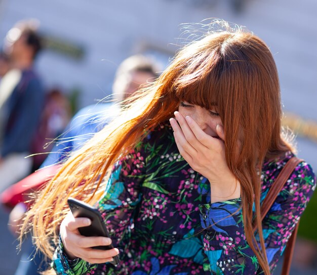 Mujer joven se ríe mirando el teléfono móvil