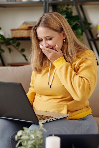 Mujer joven riendo al ver videos y memes divertidos en la pantalla del portátil