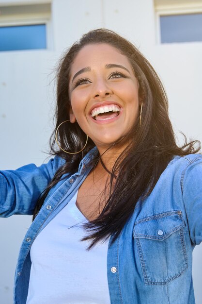 Foto mujer joven riéndose con el pelo largo con ropa informal y mirando hacia la calle soleada