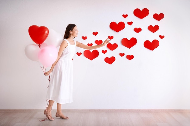 Mujer joven romántica con globos cerca de la pared decorada para el Día de San Valentín