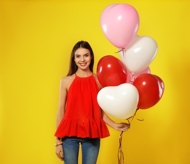 Mujer joven romántica con globos en forma de corazón para el Día de San Valentín sobre fondo de color