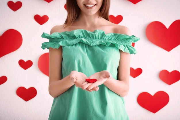 Mujer joven romántica con un pequeño corazón de fieltro cerca de la pared decorada para el Día de San Valentín