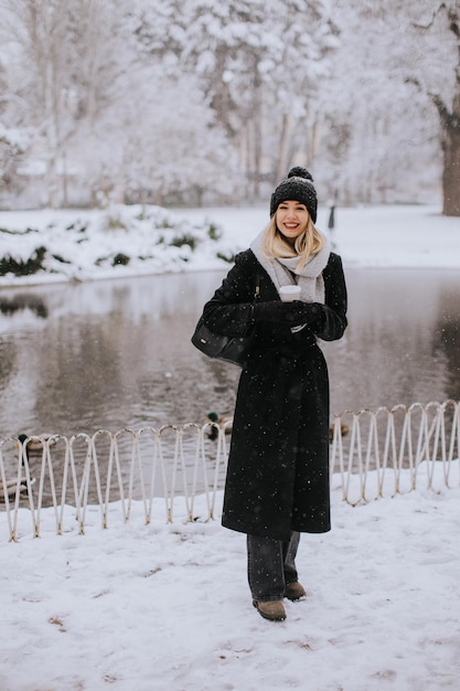 Mujer joven en ropa de abrigo disfrutando en la nieve con una taza de café para llevar