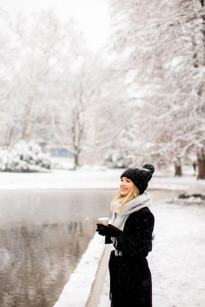 Mujer joven en ropa de abrigo disfrutando en la nieve con una taza de café para llevar