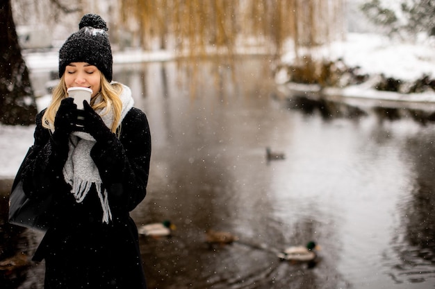 Mujer joven en ropa de abrigo disfrutando en la nieve con una taza de café para llevar