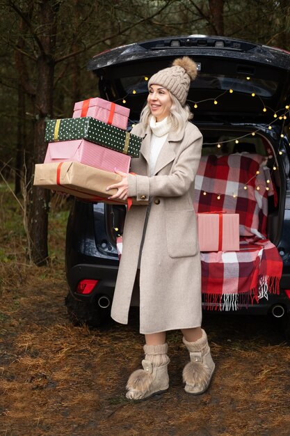 Mujer joven en ropa cálida y acogedora con cajas de regalo de Navidad cerca del coche