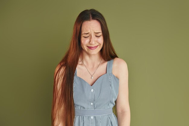 Mujer joven en ropa casual está llorando mientras está de pie en el interior del estudio