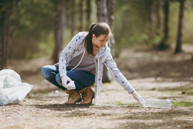 Foto mujer joven en ropa casual, guantes de limpieza de basura en bolsas de basura en el parque o el bosque. problema de la contaminación ambiental