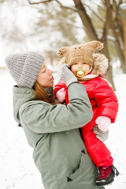 Mujer joven en ropa casual de invierno caminando con su niño pequeño en el parque cubierto de nieve cerca del río