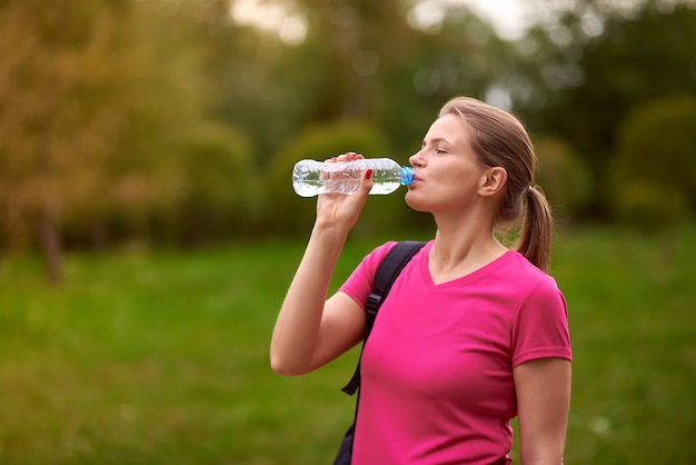 Mujer joven, en, ropa deportiva, agua potable, en el parque