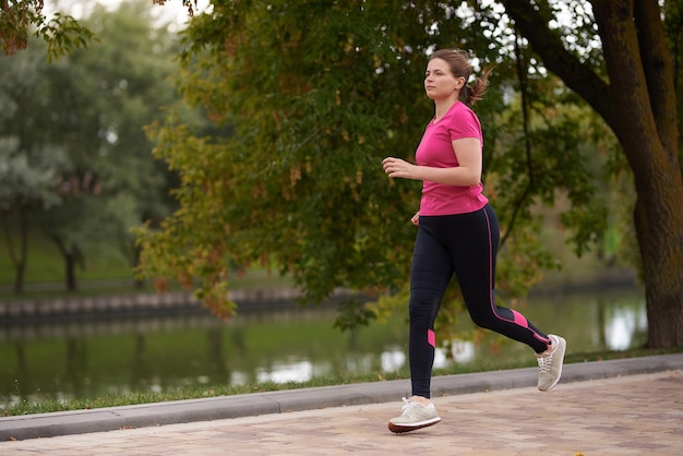 Mujer joven en ropa deportiva corre a lo largo de la ruta del parque