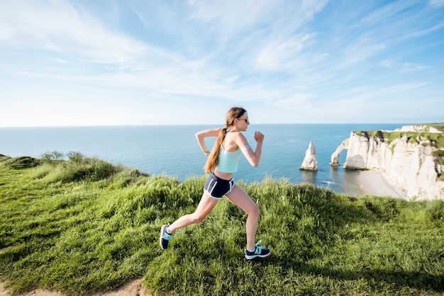 Mujer joven en ropa deportiva corriendo al aire libre en la hermosa costa rocosa con gran vista sobre el océano cerca de la ciudad de Etretat en Francia