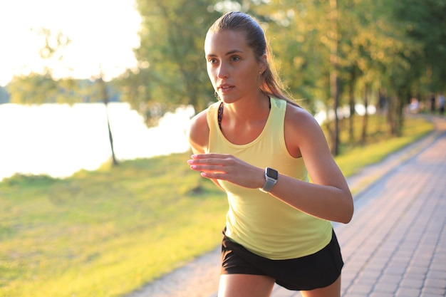 Mujer joven en ropa deportiva corriendo mientras hace ejercicio al aire libre.