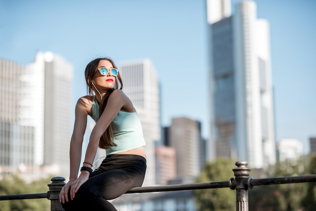 Mujer joven en ropa deportiva descansando sobre la valla durante el ejercicio matutino en la ciudad de Frankfurt